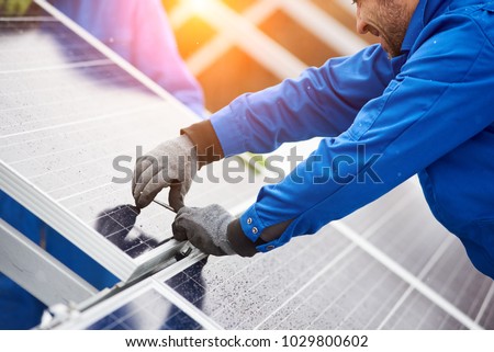 Smiling male technician in blue suit installing photovoltaic blue solar modules with screw. Man electrician panel sun sustainable resources renewable energy source alternative innovation