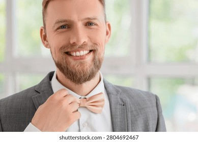 Smiling man adjusting beige bow tie in suit