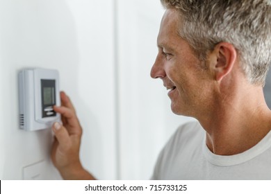 Smiling Man Adjusting Thermostat On Home Heating System