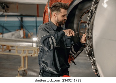 Smiling man airline maintenance technician using screwdriver while repairing airplane at repair station - Powered by Shutterstock