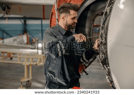 Smiling man airline maintenance technician using screwdriver while repairing airplane at repair station