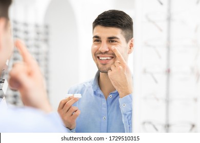 Smiling man applying contacts, looking in mirror, holding contact eye lenses container in hand, copy space - Powered by Shutterstock