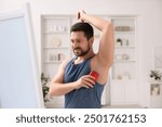 Smiling man applying solid deodorant at home