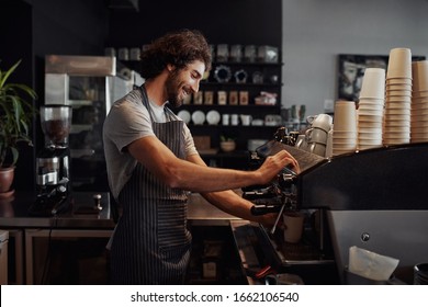 Smiling man with apron preparing coffee for customer in his small business