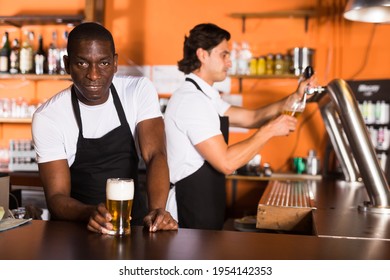 Smiling man bartender offering glass of golden beer, man pouring beer on background in bar - Powered by Shutterstock