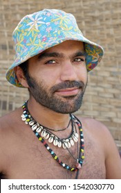 Smiling Man With A Beard On Vacation Wearing A Colourful Hat And A Cowrie Shell Necklace.