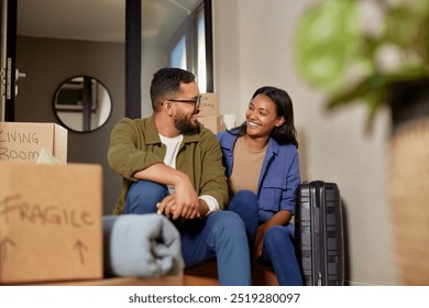 Smiling man and beautiful woman sitting on the floor after a day of moving into their new home. Mixed race couple enjoying a break together surrounded by moving boxes. Mid adult couple in new home. - Powered by Shutterstock