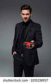 Smiling Man In Black Suit Holding Gift Box Isolated On Grey, International Womens Day Concept