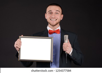 smiling man in a bow-tie with mic holding empty blank photo frame with copy space. announcing the winner. award page. prize list. appreciation. best of the year. special offer