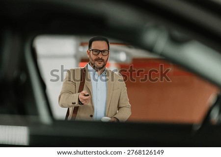Smiling man with briefcase using car remote control while walking in an underground parking garage, representing modern lifestyle and technology
