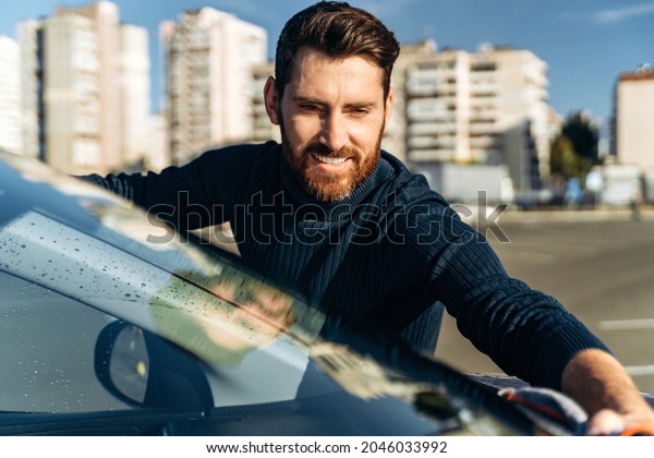Smiling man cleaning car and drying
vehicle with microfiber cloth. Hand wipe down paint surface of
shiny car after polishing. Car detailing and car wash
concept