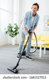 Smiling Man Cleaning Carpet With Vacuum Cleaner And Listening Music In Headphones At Home