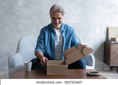 Smiling Man Consumer Open Cardboard Box Get Postal Parcel, Male Customer Receive Carton Package Sit On Sofa At Home