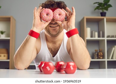 Smiling Man Covering Eyes With Sugary Doughnuts. Funny Chubby Guy Forgets About Sports Exercise And Fools Around With Pair Of Delicious Donuts. Cheat Day. Eating Sweet Food Along With Fitness Workouts