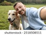 Smiling man with cute Golden Retriever dog taking selfie on spring day