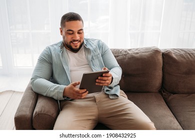 Smiling Man With Digital Tablet Sitting On A Sofa At Home