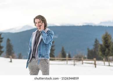 smiling man with dreadlocks talking on the phone among the snowy mountains in winter