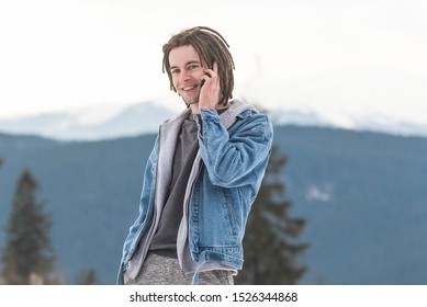 smiling man with dreadlocks talking on the phone among the snowy mountains in winter