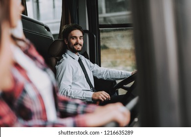 Smiling Man Driving Tour Bus. Professional Driver. Young Happy Man Wearing White Shirt Sitting On Driver Seat And Looking At Woman. Attractive Confident Man At Work. Traveling And Tourism Concept