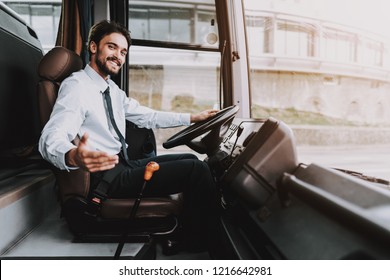Smiling Man Driving Tour Bus. Professional Driver. Young Happy Man wearing White Shirt and Black Tie Sitting on Driver Seat. Attractive Confident Man at Work. Traveling and Tourism Concept