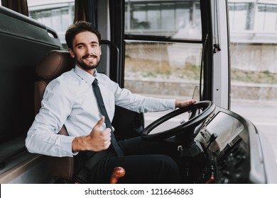 Smiling Man Driving Tour Bus. Professional Driver. Young Happy Man Wearing White Shirt And Black Tie Sitting On Driver Seat. Attractive Confident Man At Work. Traveling And Tourism Concept