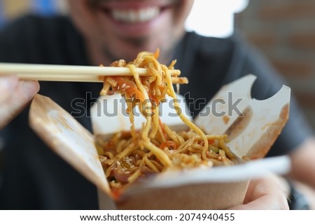 Smiling man eating spicy noodle chinese food with vegetable using chopsticks