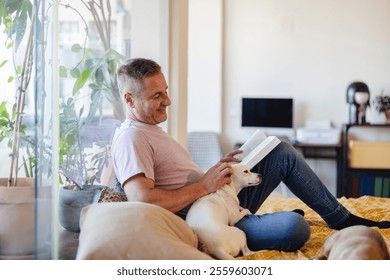 Smiling man enjoying a peaceful moment while reading a book and petting his small jack russell dog, relaxing on the bed at home, surrounded by a cozy atmosphere and natural light - Powered by Shutterstock