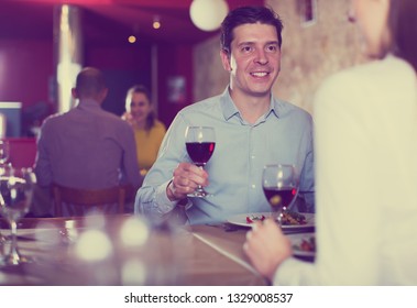 Smiling man with female partner having dinner and drinking red wine at restaurant - Shutterstock ID 1329008537