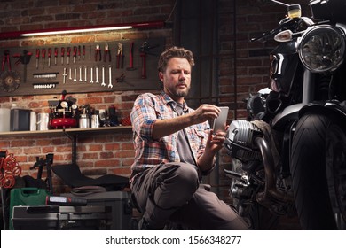 Smiling man in garage kneeling to take a close-up photo of classic vintage motorcycle with his mobile phone - Powered by Shutterstock