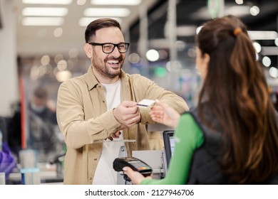 A smiling man giving credit card to a cashier and paying for groceries in supermarket.