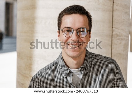 Smiling man with glasses in a houndstooth jacket standing against a textured wall, exuding casual confidence.