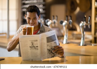 Smiling man having beer while reading newspaper in a restaurant - Powered by Shutterstock