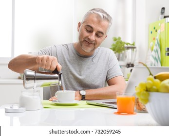 Smiling man having an healthy breakfast at home, he is sitting at the kitchen table and pouring coffee in a cup - Powered by Shutterstock