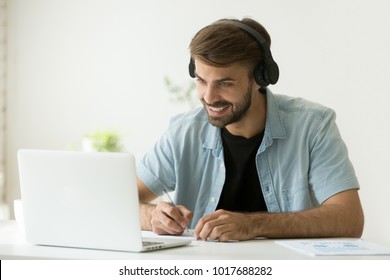 Smiling Man In Headphones Looking At Computer Screen Watching Webinar, Making Business Video Call, Young Businessman Consulting Remote Client Online Writing Notes, Hr Holding Distance Job Interview