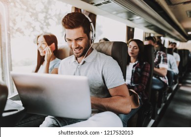 Smiling Man in Headphones Using Laptop in Tour Bus. Young Handsome Man Sitting on Passenger Seat of Tourist Bus and Typing on Laptop. Traveling and Tourism Concept. Happy Travelers on Trip