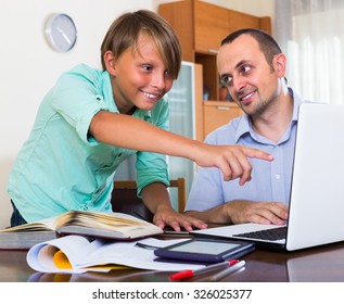 Smiling Man Helping Teenage Son To Do Homework At Home 