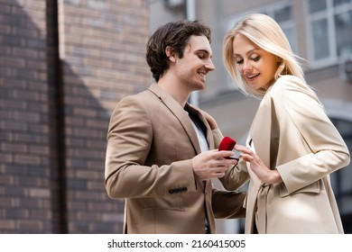 smiling man holding jewelry box while making marriage proposal to blonde woman