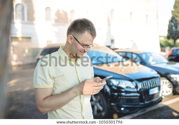 smiling man\
holding mobile phone standing at\
car