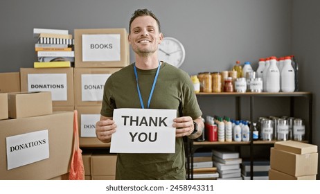 A smiling man holding a 'thank you' sign surrounded by donation boxes in an indoor charity center.
