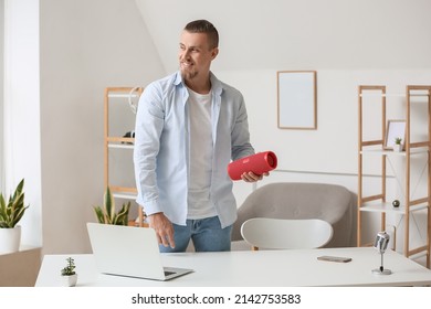 Smiling Man Holding Wireless Portable Speaker Near Table In Room