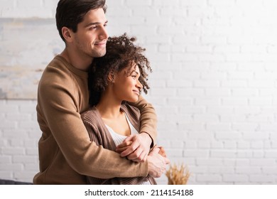 Smiling man hugging curly african american girlfriend at home - Shutterstock ID 2114154188