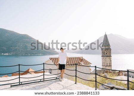 Smiling man leans on a rope fence on an observation deck near the church bell tower. Perast, Montenegro