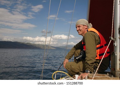 The Smiling Man In A Life Jacket Sits On A Nose Of The Yacht Floating On The Lake Sevan Armenia