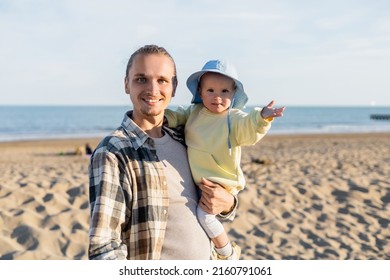 Smiling Man Looking At Camera While Holding Baby Daughter On Beach In Treviso