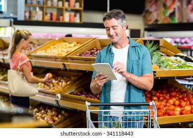 Smiling man looking at the grocery list at the supermarket - Powered by Shutterstock