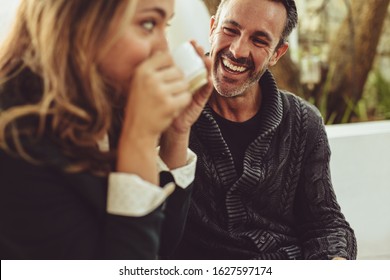 Smiling man looking at his girlfriend drinking coffee. Couple sitting at coffee shop.