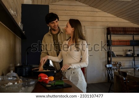 Smiling man looks at his wife, who is cooking dinner on the stove in the kitchen. 