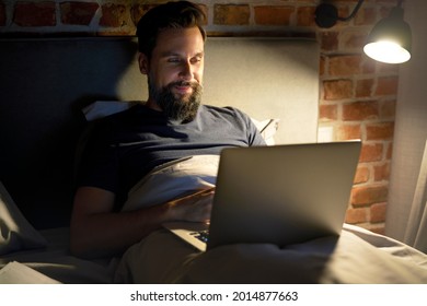 Smiling Man Lying In Bed And Using Laptop