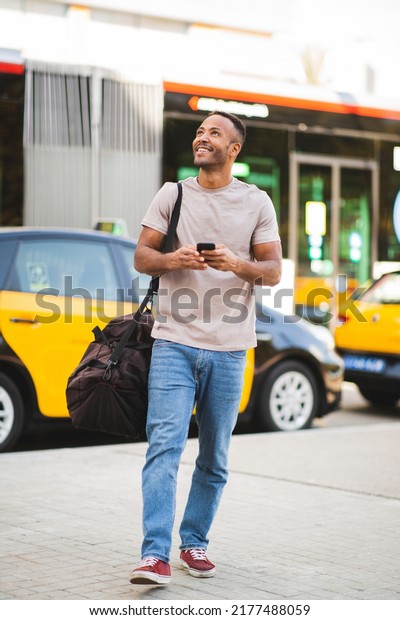 Smiling man with mobile phone and bag looking up\
outdoors in city