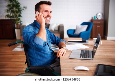 Smiling Man On Wheelchair Talking By Mobile Phone In Home Office